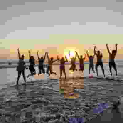 Group of travellers jumping in the air for photo at sunset on the beach.