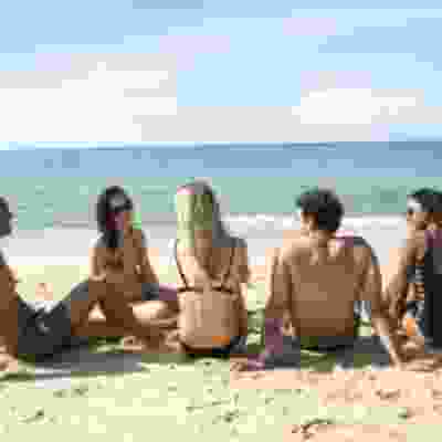 Group of travellers sat smiling on the beach shore of Langakawi.