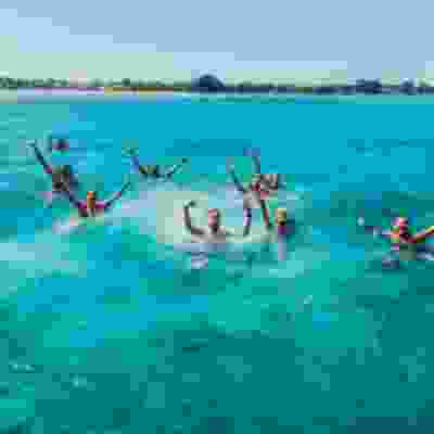 Travellers swimming in the ocean with their hands in the air on boat trip in Lombok.