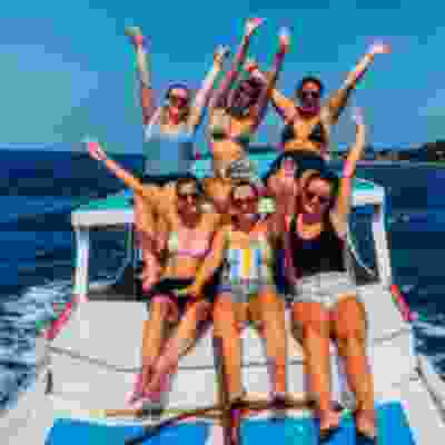 Women travellers with their hands in the air sat on the back of boat trip in Sumbawa.