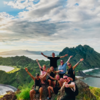 Travellers smiling with hands in the air at top of viewpoint after hike on Komodo island.