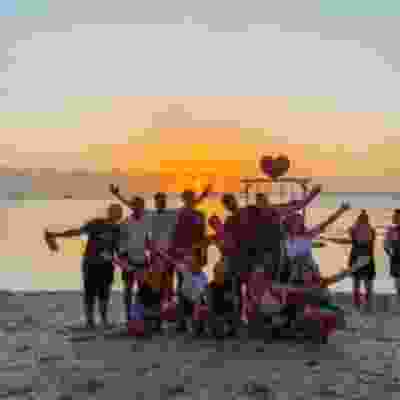 Travellers taking group photo with their hands in the air on the beach at sunset.