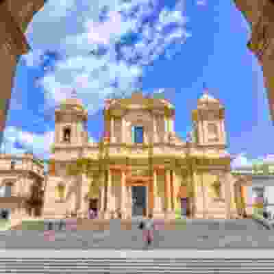 The front view of Noto Cathedral through an archway.