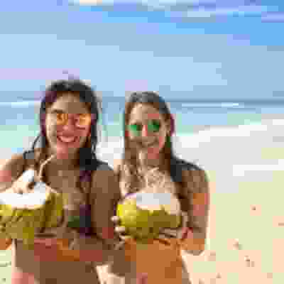 Two women smiling on the beach holding coconut drinks on Gili island.