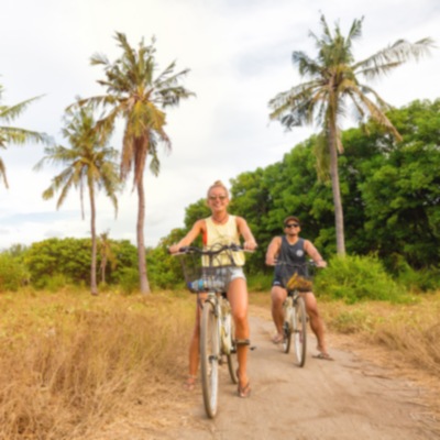 A couple smiling whilst cycling on a bike tour through palm trees on Gili T.
